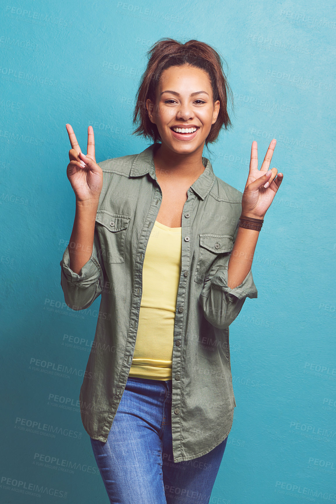 Buy stock photo Happy woman, portrait and peace sign with fashion for style, love or care on a blue studio background. Female person, brunette or model with smile, emoji or calm attitude in cool casual clothing