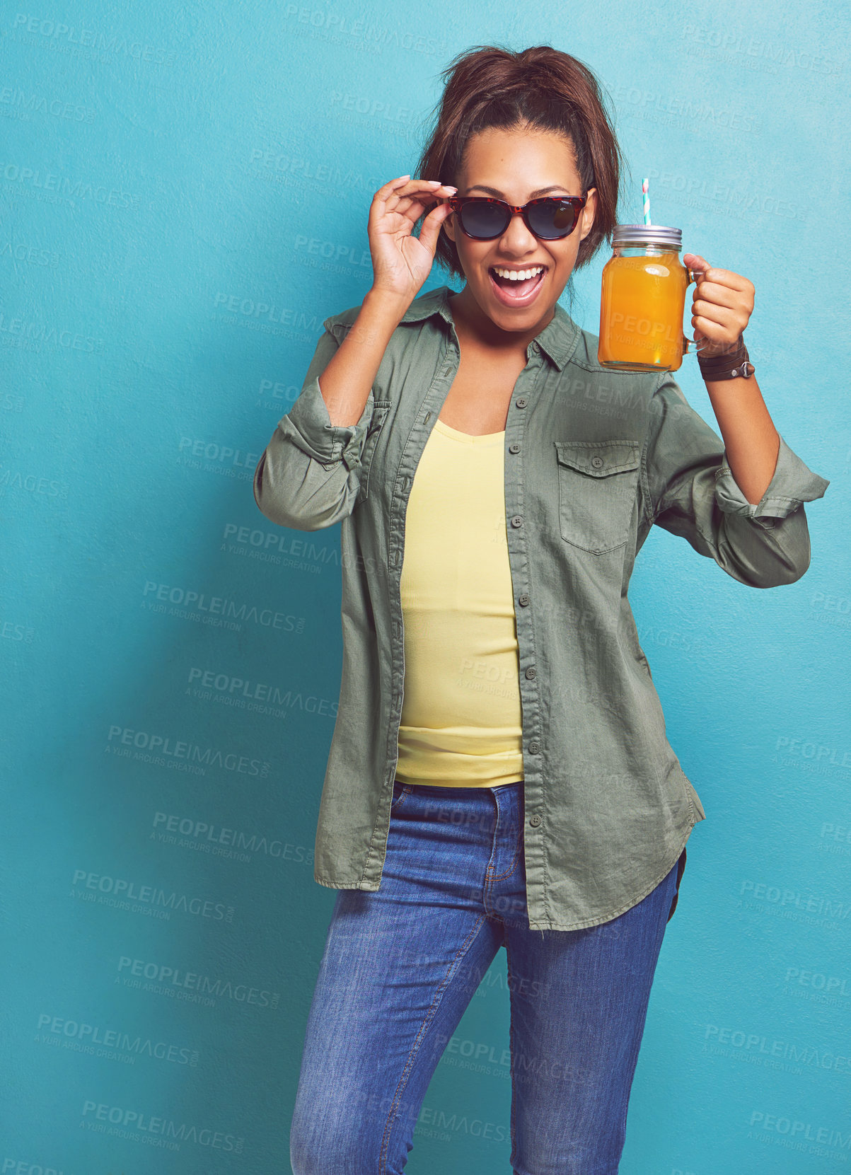 Buy stock photo Portrait of a young woman holding a juice jug against a blue background