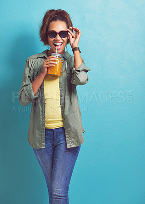Buy stock photo Excited woman, portrait and sunglasses with orange juice in fashion for vitamin C on a blue studio background. Female person, brunette or model with smile for citrus drink or fresh beverage on mockup