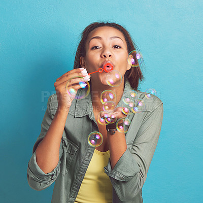 Buy stock photo Happy woman, portrait and blowing with bubble wand for soap, fun or playing with magic on a blue studio background. Young female person or model with floating liquid particles in party or celebration