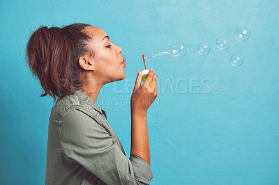 Buy stock photo Cropped shot of a young woman blowing bubbles against a blue background