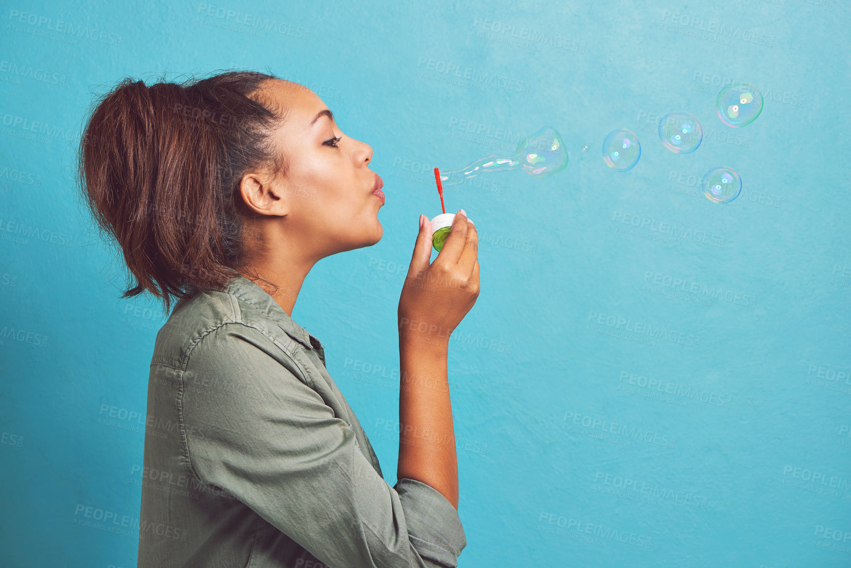 Buy stock photo Cropped shot of a young woman blowing bubbles against a blue background