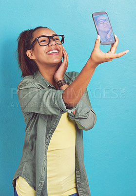 Buy stock photo Happy woman, nerd and fashion with selfie for picture, memory or review on a blue studio background. Young female person, model or geek with smile or glasses for social media, moment or photography