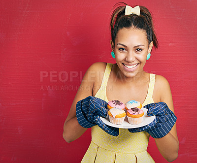 Buy stock photo Studio shot of a young woman holding a plate of cupcakes against a red background