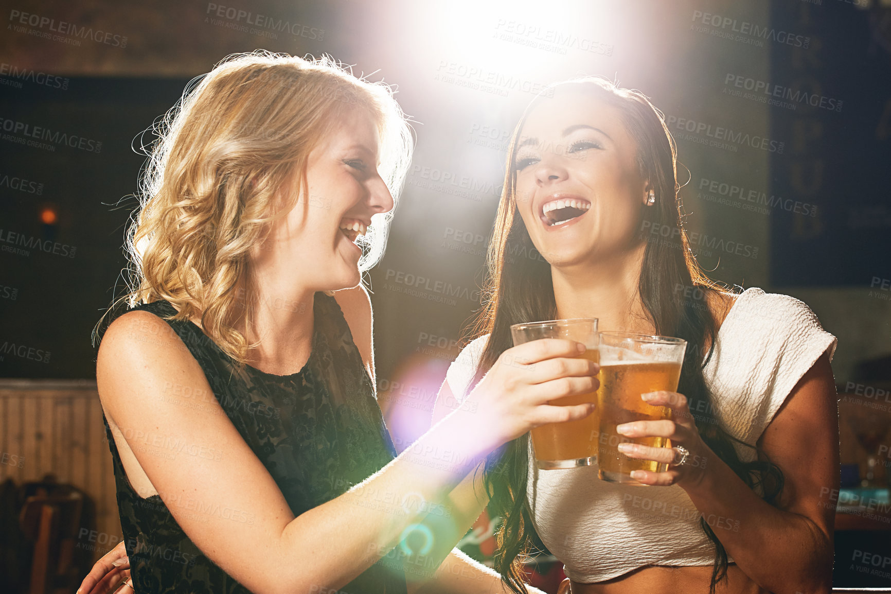 Buy stock photo Shot of two young women enjoying a beer together in a nightclub