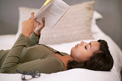 Buy stock photo Shot of a young woman reading a book while lying on bed