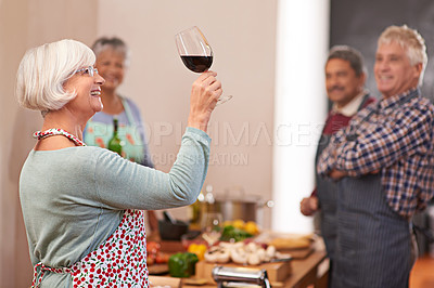 Buy stock photo Shot of a senior woman looking at her wine with friends in the background