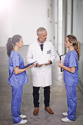 Buy stock photo Full length shot of a mature doctor teaching two female interns in the hospital corridor