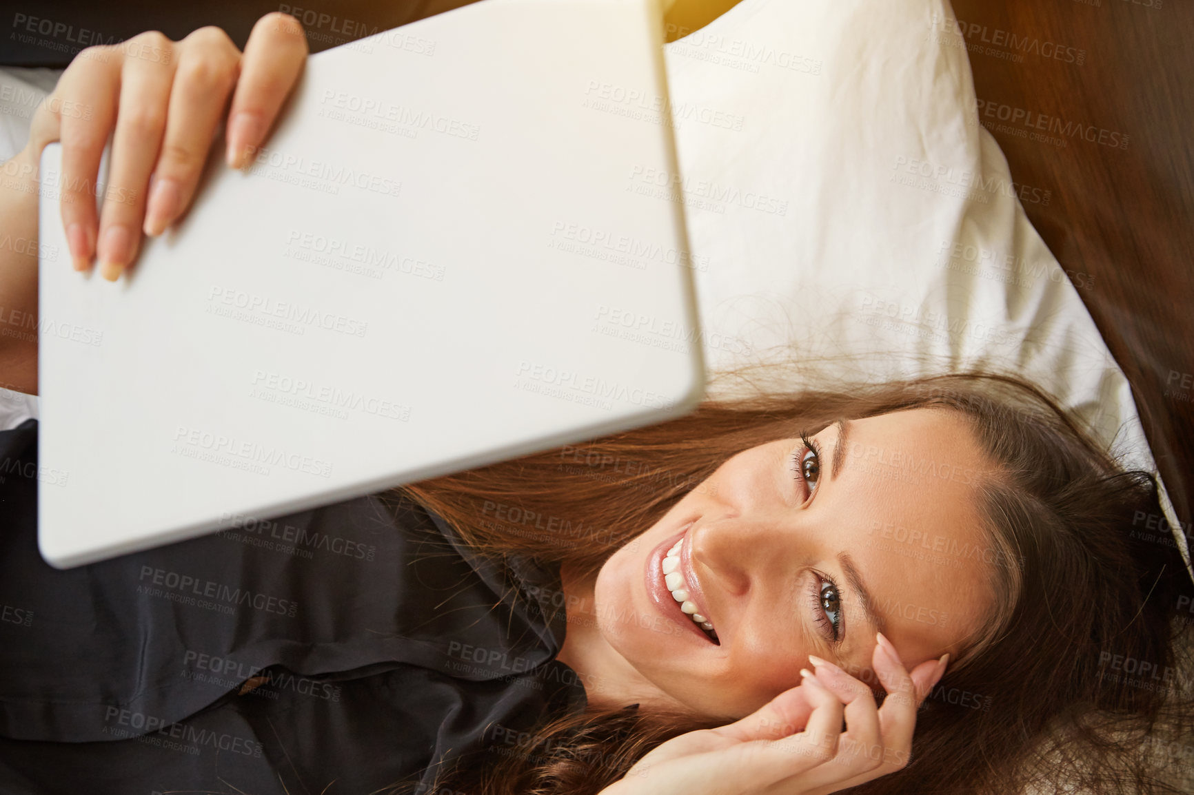 Buy stock photo Cropped shot of a young woman using her digital tablet while lying on her bed