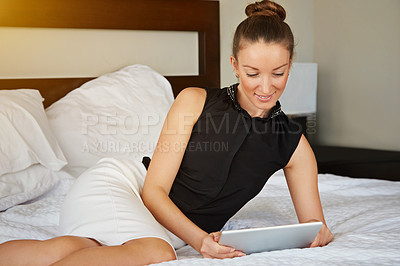 Buy stock photo Shot of a young woman using a digital tablet while lying on a bed