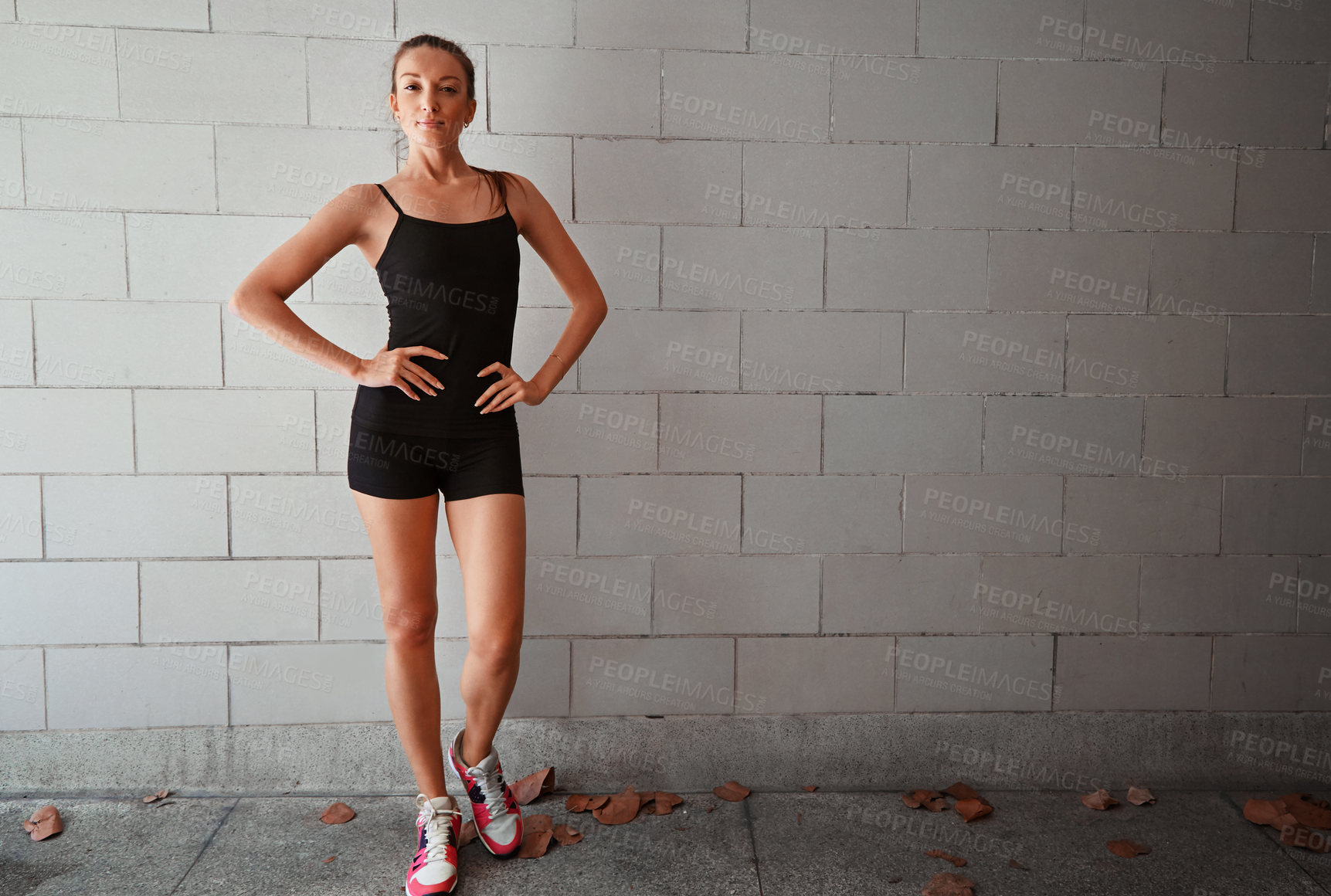 Buy stock photo Full length portrait of a sporty young woman standing with her hands on her hips against a wall