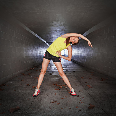 Buy stock photo Full length portrait of a sporty young woman stretching in a tunnel