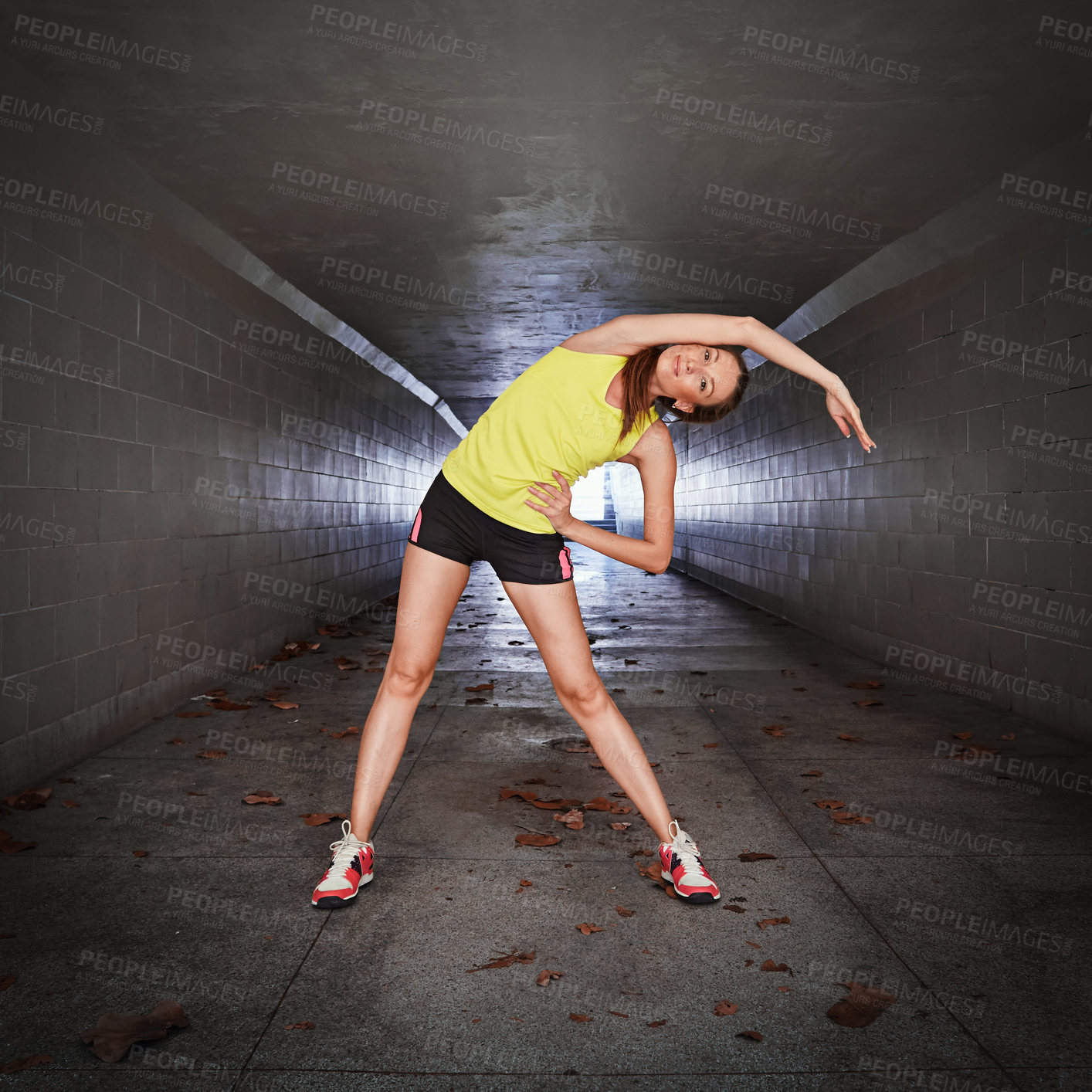 Buy stock photo Full length portrait of a sporty young woman stretching in a tunnel