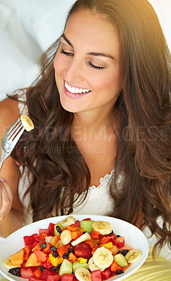 Buy stock photo Shot of a young woman eating a fruit salad on her bed