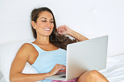 Buy stock photo Shot of a young woman using a laptop while lying on her bed