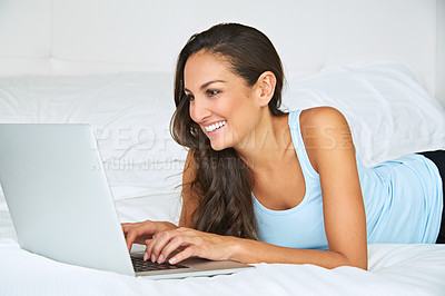 Buy stock photo Shot of a young woman using a laptop while lying on her bed