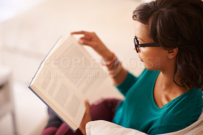 Buy stock photo Shot of a young woman reading a book on the sofa at home