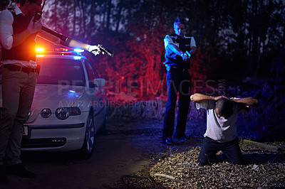 Buy stock photo Shot of policemen pointing their guns at a suspect kneeling on the ground