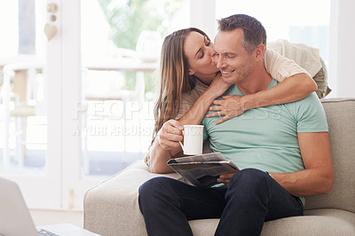 Buy stock photo Happy couple, kiss and newspaper with coffee in home, romantic and bonding together with love in marriage. Man, woman and surprise by touch with relax, warm drink and care by sofa in modern apartment