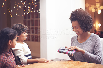 Buy stock photo Mother, kids and happy in table with gift as birthday present with care, support and bonding. Home, parents and siblings with smile together in living room as family on holiday with childhood memory