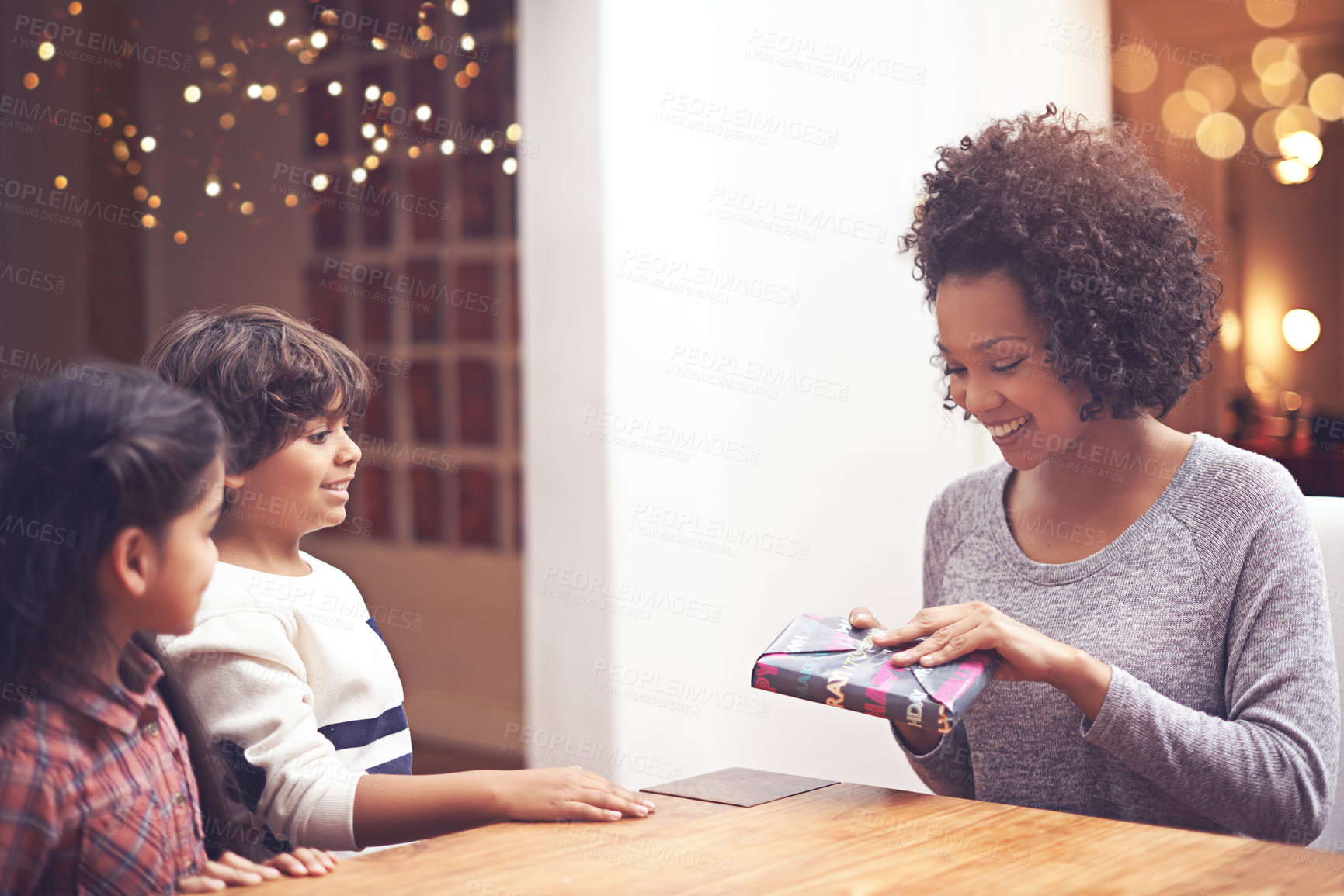 Buy stock photo Mother, kids and happy in table with gift as birthday present with care, support and bonding. Home, parents and siblings with smile together in living room as family on holiday with childhood memory