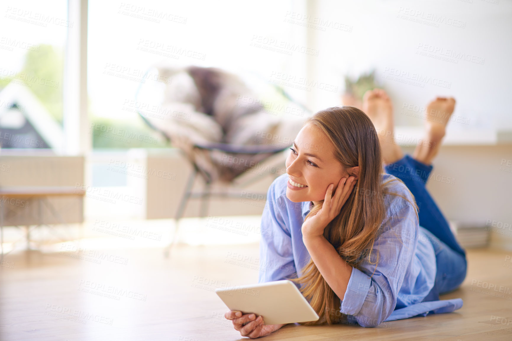 Buy stock photo Shot of a young woman using a digital tablet while lying on the floor at home