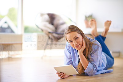Buy stock photo Shot of a young woman using a digital tablet while lying on the floor at home