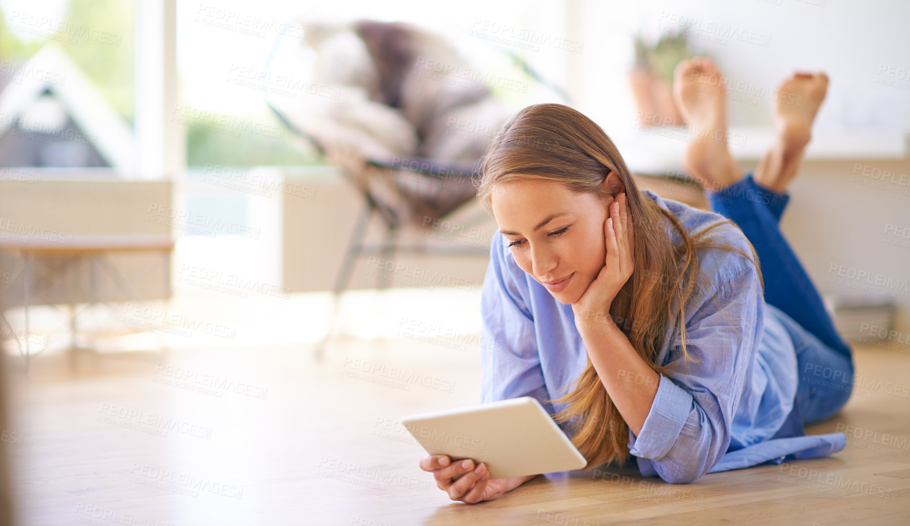 Buy stock photo Shot of a young woman using a digital tablet while lying on the floor at home