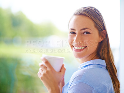 Buy stock photo Cropped portrait of a young woman having coffee while standing by a window