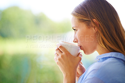 Buy stock photo Cropped shot of a young woman having coffee while standing by a window
