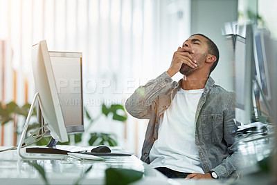 Buy stock photo Shot of a young designer yawning while working at his computer in an office