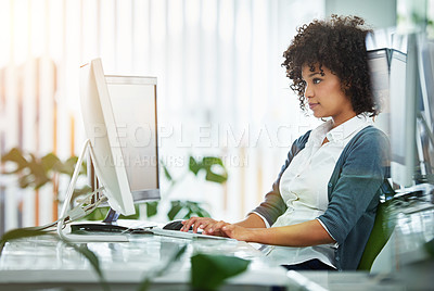 Buy stock photo Young female designer working at her computer by a desk in a modern office. Creative business woman in design typing  advertising and marketing designs on her pc keyboard at the workplace