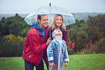Buy stock photo Family, happy and outdoor in rain with umbrella in nature for fun, happiness or quality time. Man, woman and excited child with cover for water drops with freedom, love and care while playing at park