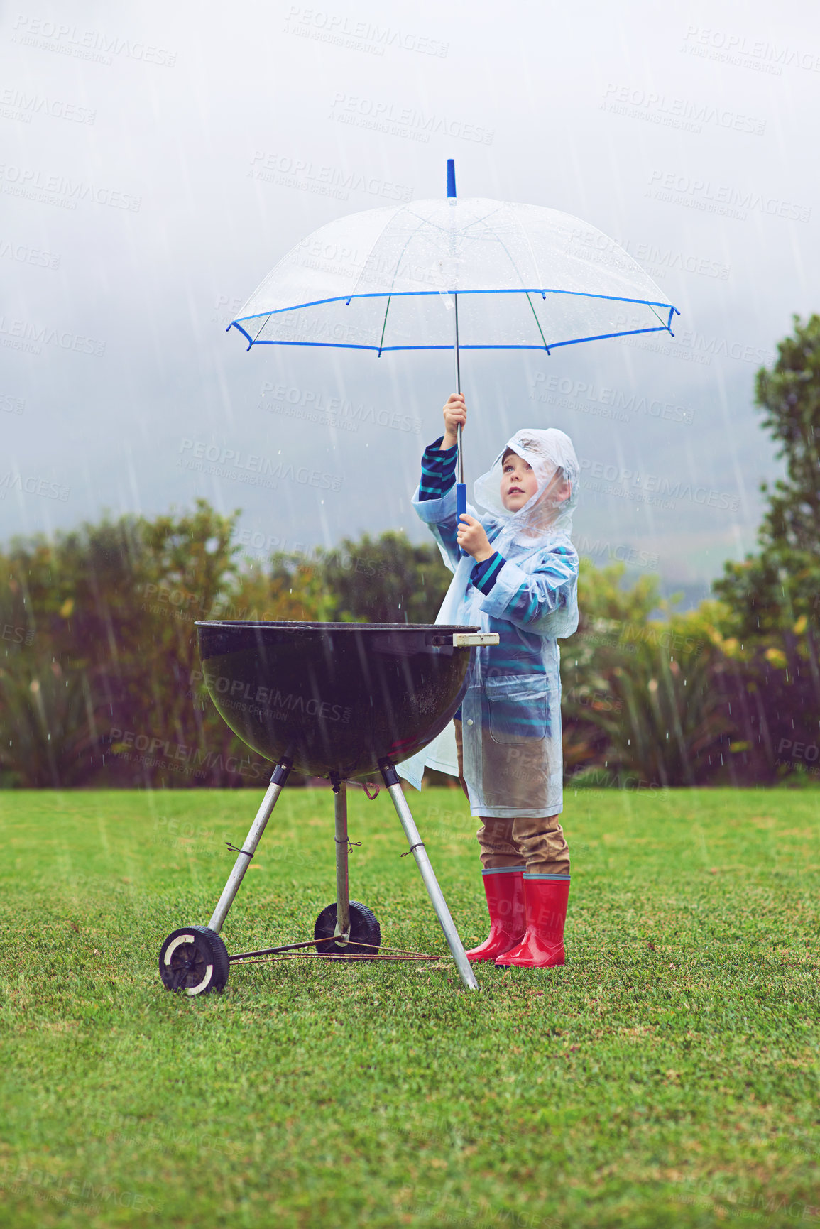 Buy stock photo Rain, umbrella and a boy covering a barbecue outdoor on a field while cooking food alone in winter. Raincoat, kids and insurance with a young male child trying to protect a bbq during stormy weather