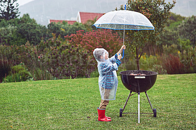 Buy stock photo Full length shot of a young boy standing in front of an outdoor grill in the rain