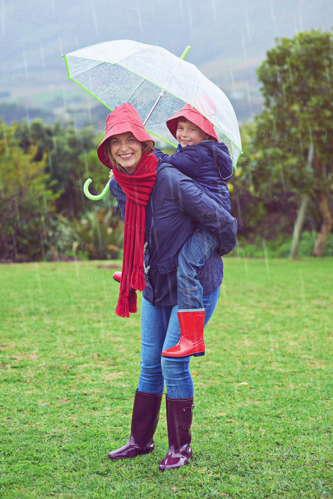 Buy stock photo Cropped portrait of a mother carrying her son on her back outside in the rain