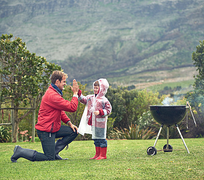 Buy stock photo Shot of a father giving his son a high five while they're having a barbecue outside