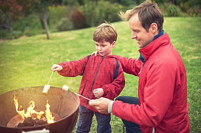Buy stock photo Shot of a father and son roasting marshmallows over a fire