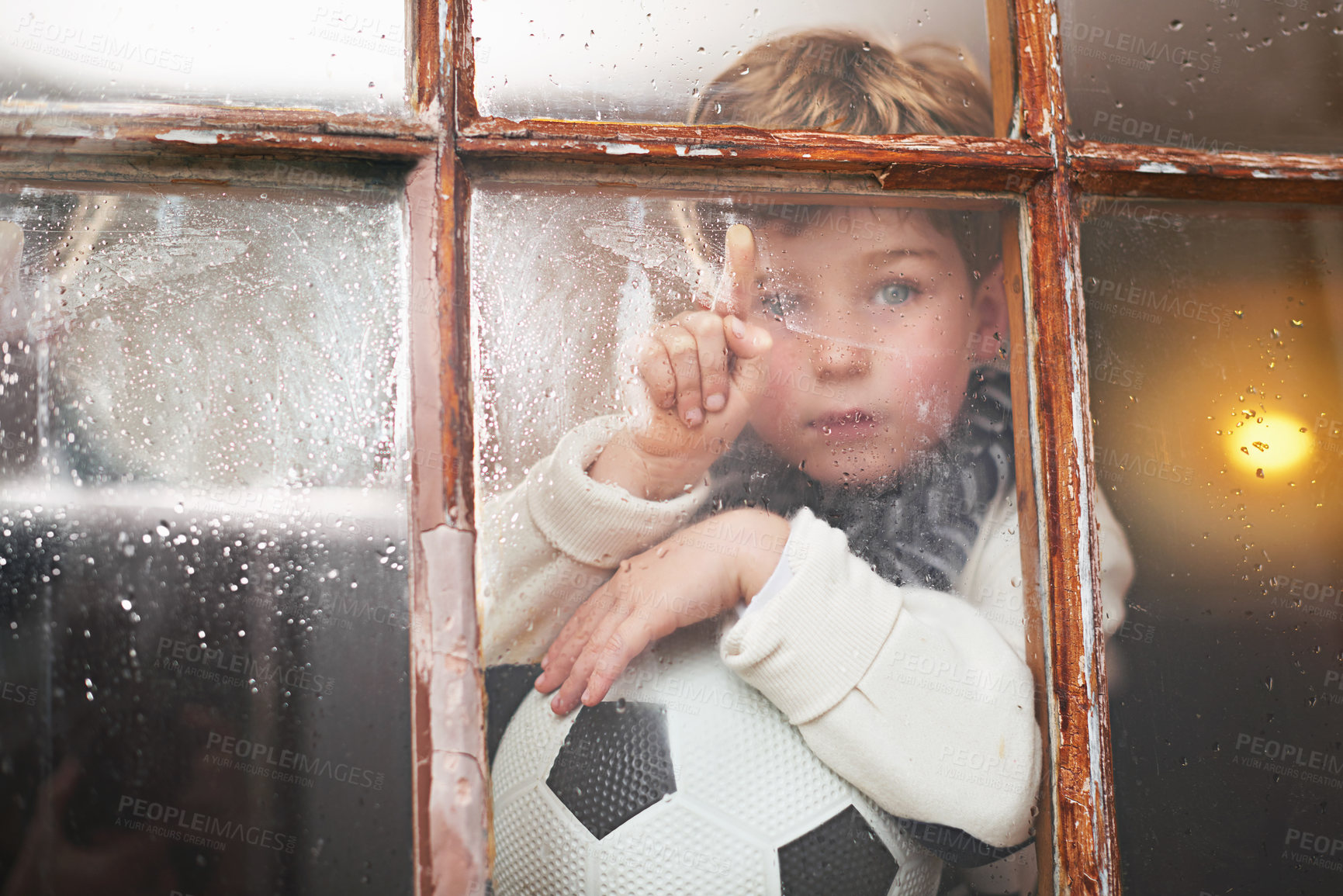 Buy stock photo A young boy sitting by the window and looking bored while it rains outside