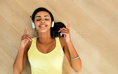 Buy stock photo High angle shot of a young woman listening to music while lying on a wooden floor