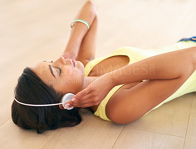Buy stock photo Shot of a young woman listening to music while lying on a wooden floor