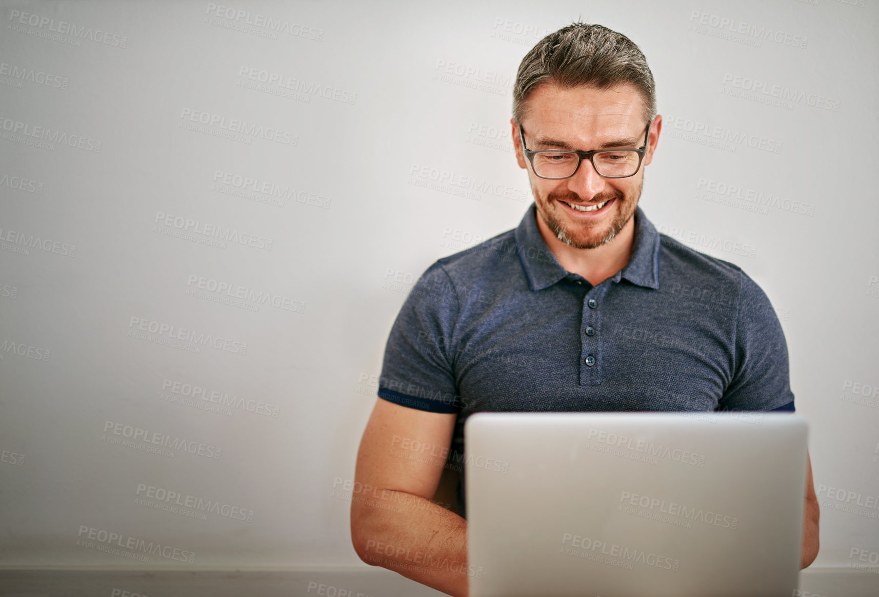 Buy stock photo Shot of a man using his laptop while sitting against a gray wall