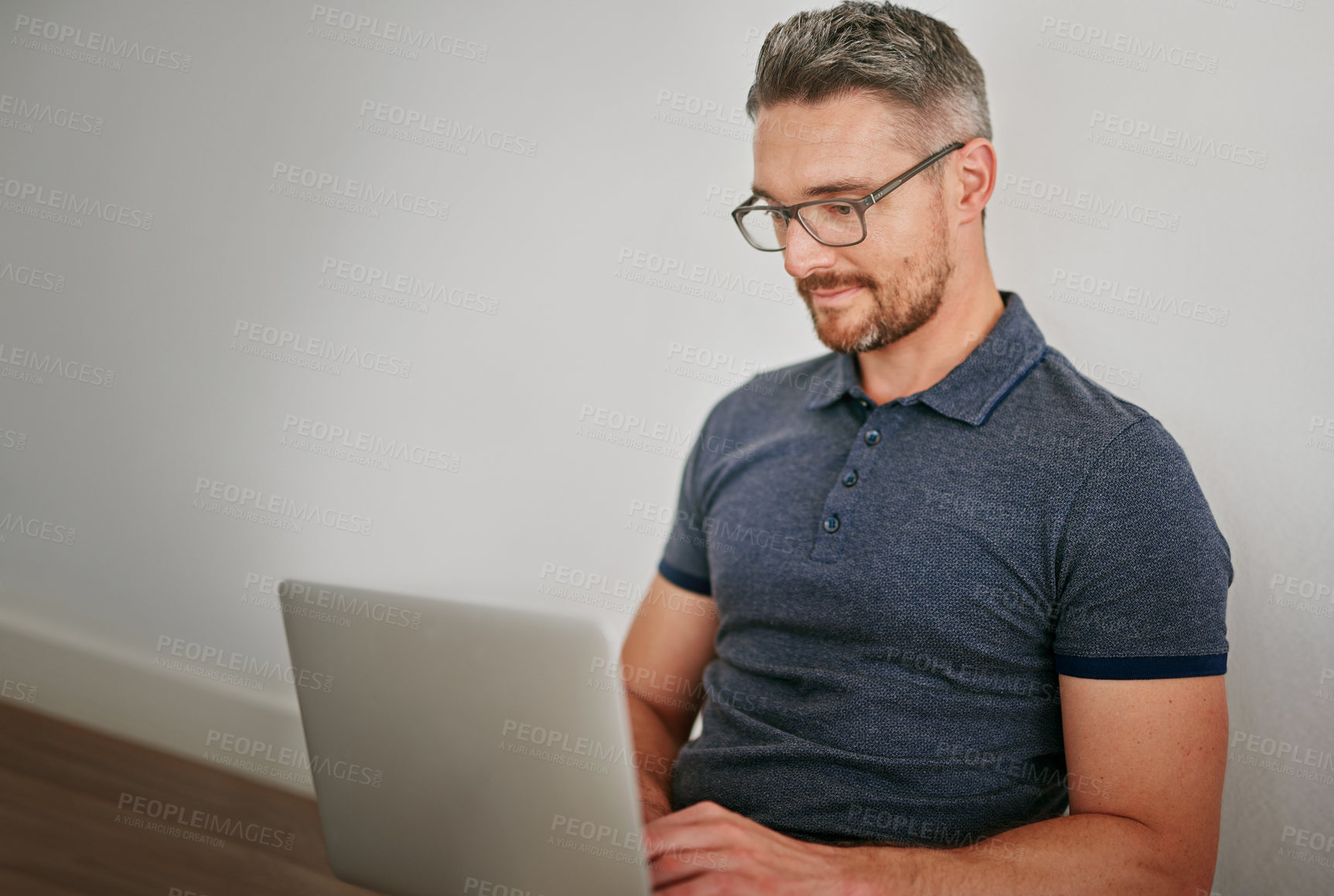 Buy stock photo Shot of a man using his laptop while sitting against a wall