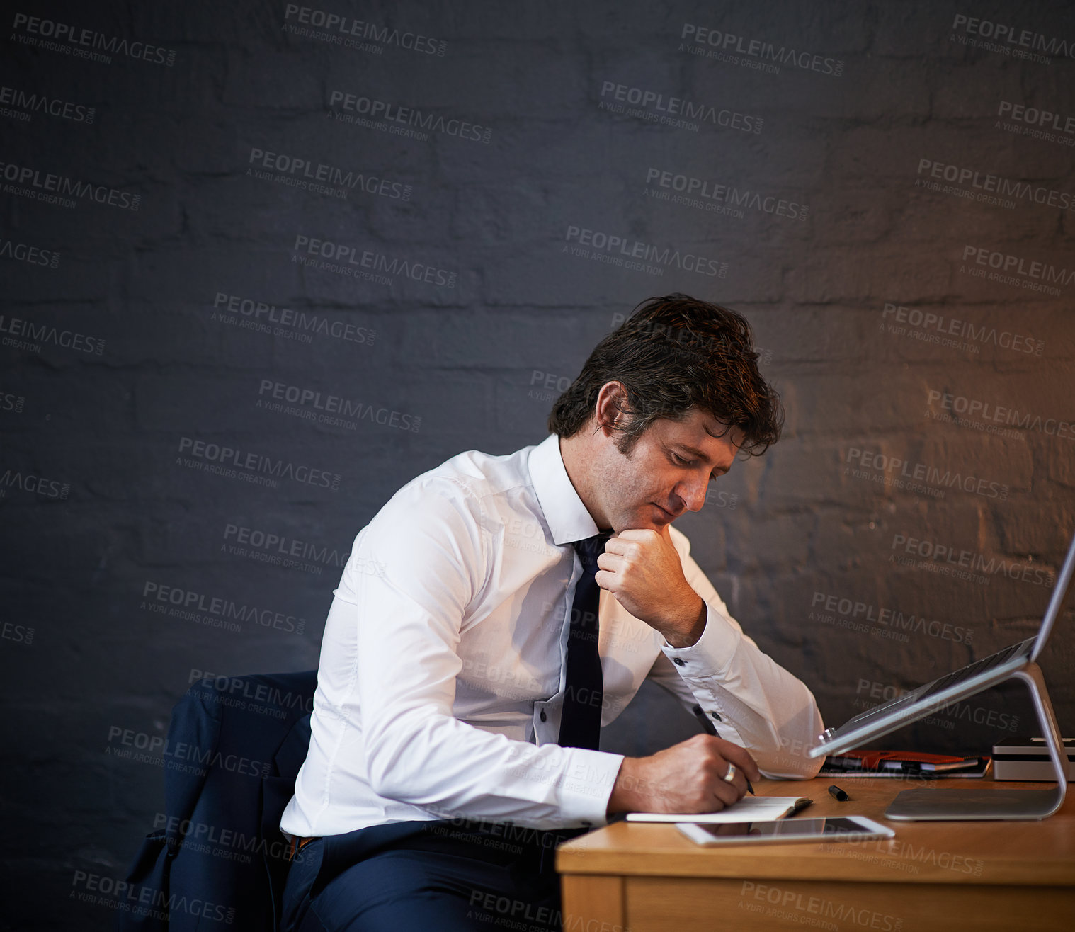 Buy stock photo Desk, investigation and writing with detective man in office at night to work on criminal report. Brick wall, laptop and notebook with mature investigator at table for evidence, justice or research