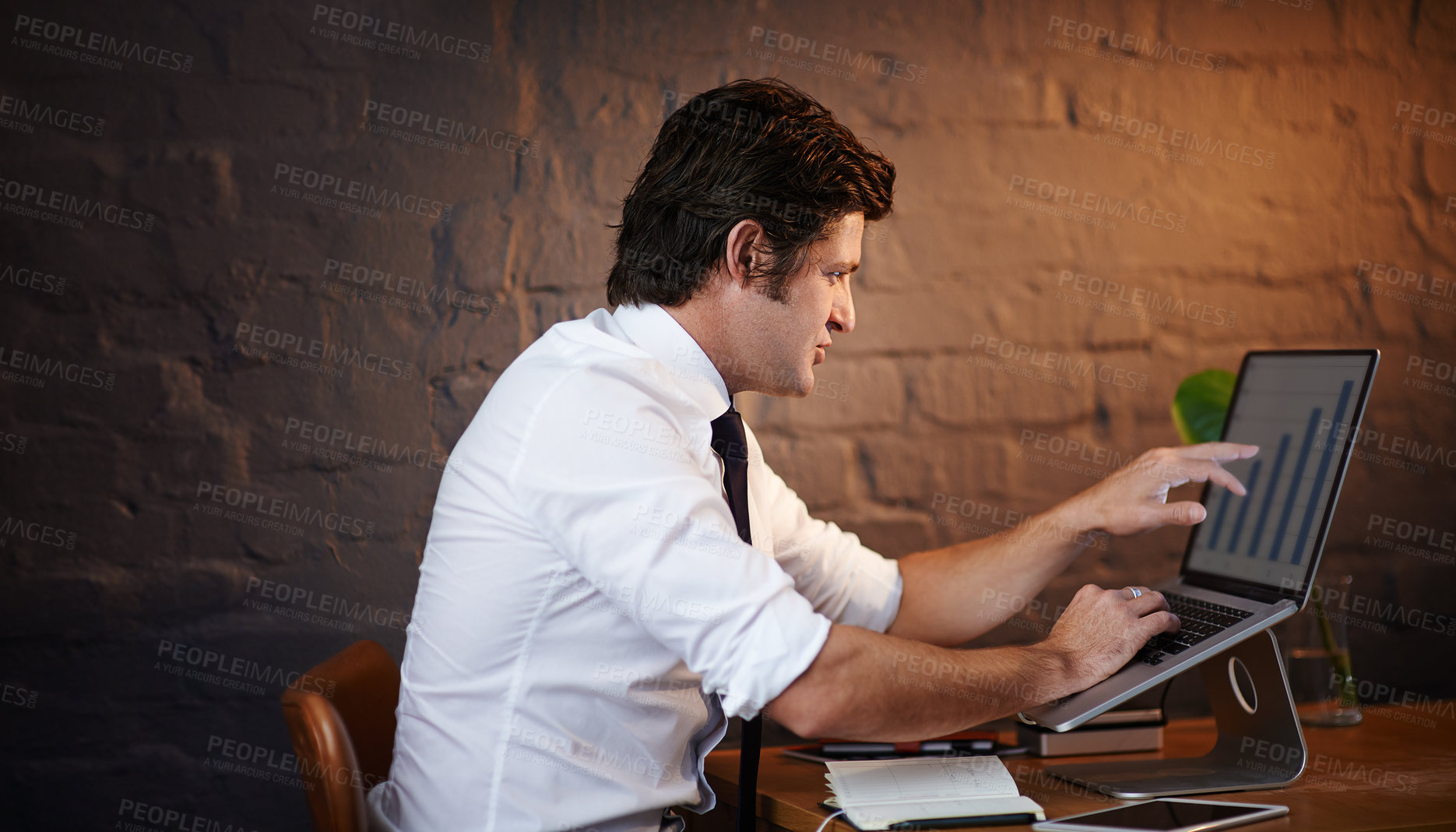 Buy stock photo Desk, finance and investigation with detective man in office at night to work on fraud case. Brick wall, data and laptop with mature investigator at table for evidence review, justice or research