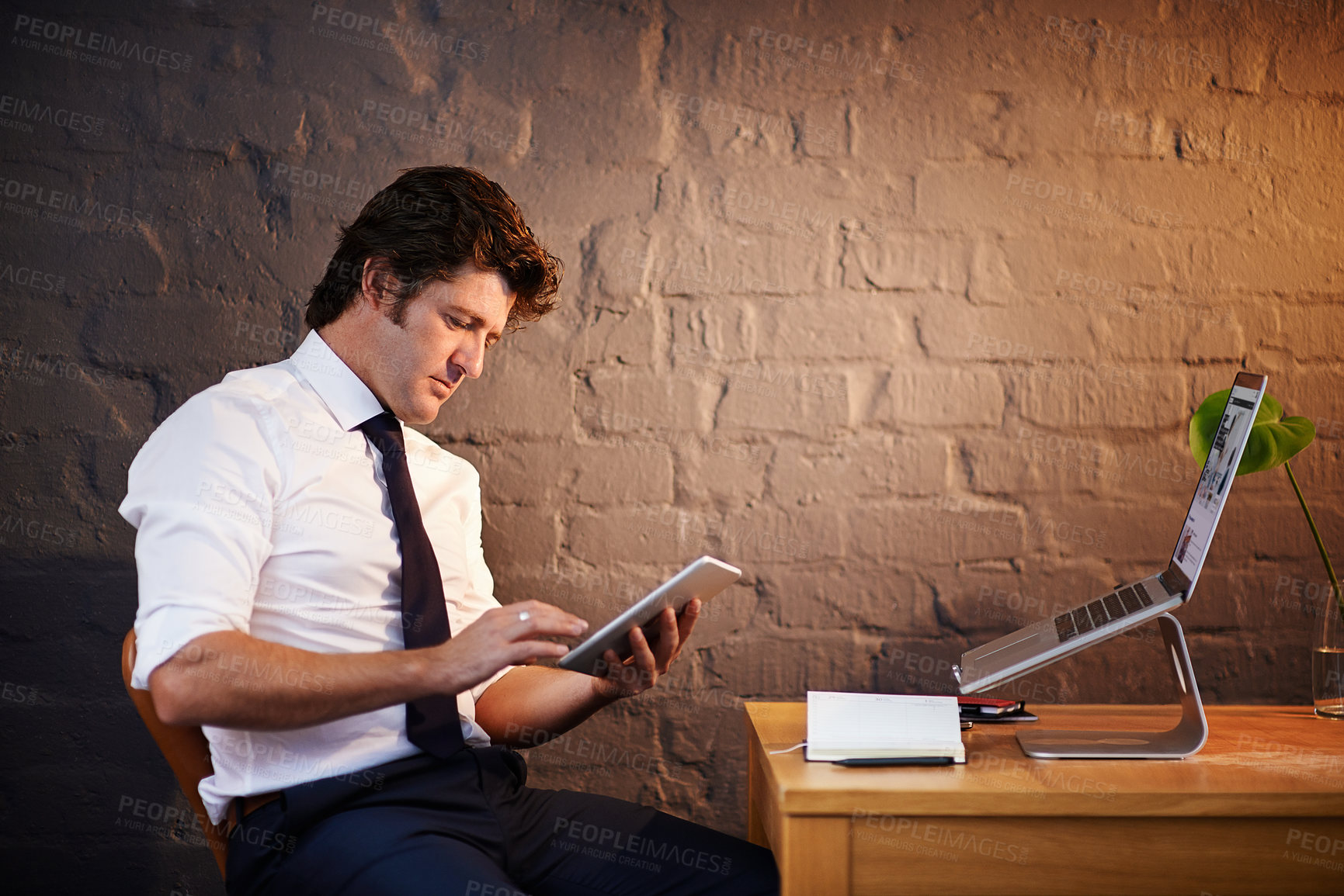 Buy stock photo Desk, investigation and technology with detective man in office at night to work on criminal report. Brick wall, laptop and tablet with mature investigator at table for evidence, justice or research