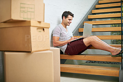 Buy stock photo Shot of a young man using his laptop while in the process of moving house