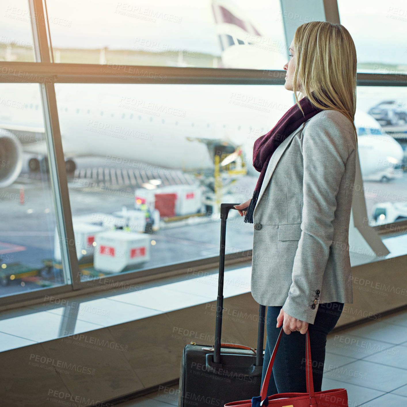 Buy stock photo Shot of a young woman standing in an airport looking out the window