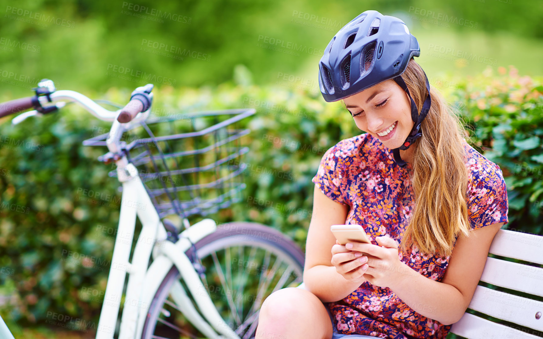 Buy stock photo Phone, bicycle and woman on bench in park with helmet, smile and online chat with connectivity. Communication, relax and happy girl checking social media with bike, smartphone or mobile app in nature