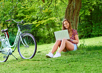 Buy stock photo Shot of a young woman using a laptop in the park